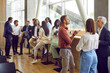 © Studio Romantic - Full length photo of a group of diverse business people men and women chatting after meeting. Company employees or group of staff talking in modern office or conference room discussing work project.