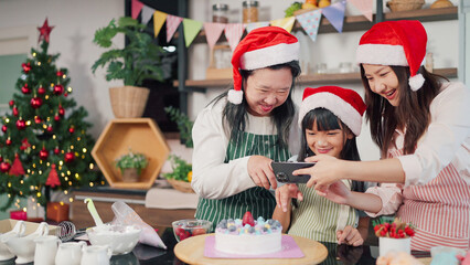 Happy Grandmother, mother and little daughter taking photo through smartphone while finish decorated cake for Christmas day. Three generations Asian women taking selfie through smartphone