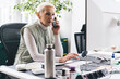 © BullRun - Focused senior woman sitting at table and talking on smartphone