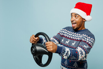 Wall Mural - Side view young surprised man wear knitted sweater Santa hat posing hold steering wheel driving car isolated on plain pastel blue background. Happy New Year 2024 celebration Christmas holiday concept.