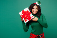 Merry Little Kid Teen Girl Wear Hat Casual Clothes Posing Hold Present Box With Gift Ribbon Bow Look Aside Isolated On Plain Green Background Studio Portrait. Happy New Year Christmas Holiday Concept.