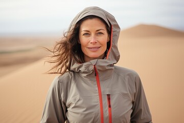 Canvas Print - Portrait of a tender woman in her 40s wearing a functional windbreaker against a serene dune landscape background. AI Generation