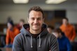 © CogniLens - Portrait of a happy man in his 30s wearing a zip-up fleece hoodie against a lively classroom background. AI Generation