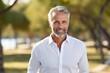 © CogniLens - Portrait of a tender man in his 50s wearing a classic white shirt against a bright and cheerful park background. AI Generation
