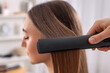 © New Africa - Hairdresser straightening woman's hair with flat iron in salon, selective focus