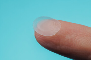 close-up round acne patch on finger on blue background. acne patches for treatment of pimple and ros