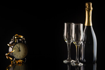 Champagne bottle and two glasses on a black background with a clock. New Year and Christmas celebration concept.