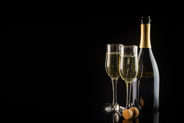 Two glasses of champagne and bottle on a black background with copy space. New Year and Christmas celebration concept.