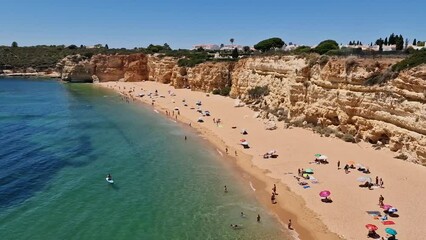 Canvas Print - Delightful paradisiacal Portuguese beach with turquoise water clean sand and vacationing tourists. To the south in the town of Armacao de Pera