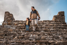 Photographer Man And His Fashionable Little Son Sightseeing Together In A Castle Walking Down Stairs Hand In Hand While Looking At The Surroundings, Traveling And Photographing A Small Town