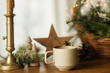 Wall Mural - Stylish cup of warm tea, fir branches in basket, wooden trees and star, pine cones and lights on table. Modern christmas rustic eco friendly decor, scandinavian winter hygge. Atmospheric christmas