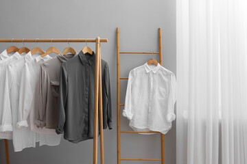 Wall Mural - Different stylish shirts hanging on ladder and rack near grey wall in room. Organizing clothes