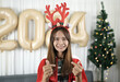 © buraratn - Asian woman dressed as a shanty Smiling happily waiting to celebrate Christmas 2024. Decorate and decorate the room with a Christmas tree and 2024 balloons.