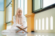 © maya1313 - The image of an Asian Muslim woman in the Islamic religion in hijab in cream color. reading the Quran and having a happy Staying in a beautiful mosque, Arabic word translation: The Holy Al Quran.