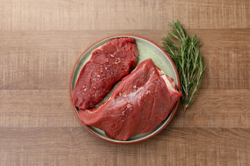 Pieces of raw beef meat with spices and rosemary on wooden table, flat lay