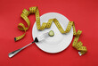 Plate with cucumber slice, measuring tape and fork on red background, top view. Diet concept