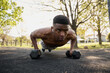 © StratfordProductions - Shirtless young black man with wireless earphones doing push-ups with dumbbells in park