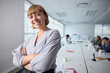 © StratfordProductions - Young businesswoman in businesswear smiling and looking at camera with arms crossed in office