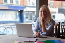 Smiling Freelancer With Note Pad And Laptop In Coffee Shop