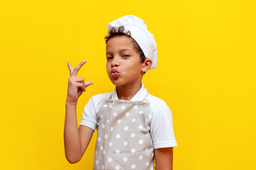 african american boy in chef's uniform and hat shows an italian gesture on yellow isolated background