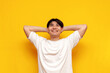 © Богдан Маліцький - happy young asian guy in a white t-shirt resting and dreaming on a yellow isolated background