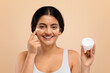 © Prostock-studio - Skincare Routine. Happy Young Indian Woman Applying Moisturizing Cream On Face,