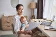 © Seventyfour - Portrait of young mother with baby working from home and reviewing documents, copy space