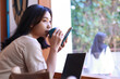 © M Alfan Setyawan - happy asian woman sit in cafe drink a cup of coffe and using smartphone with laptop on table wearing fashionable clothes, beautiful female work from coffee shop, relaxation