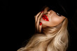 Beautiful blonde woman in elegant black hat and red lips posing sensually on a black background.