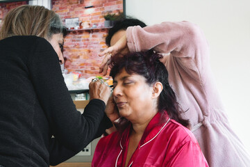 A middle-aged woman having her hair and makeup done by a couple of her female friends in a domestic living room at home