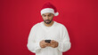© Krakenimages.com - African american man wearing christmas hat using smartphone over isolated red background