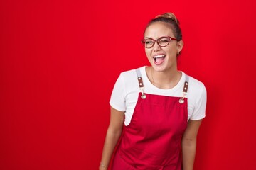 Sticker - Young hispanic woman wearing waitress apron over red background winking looking at the camera with sexy expression, cheerful and happy face.