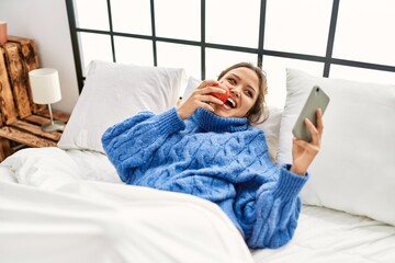 Wall Mural - Young beautiful hispanic woman using smartphone eating apple at bedroom