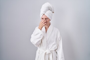 Canvas Print - Blonde caucasian woman wearing bathrobe smelling something stinky and disgusting, intolerable smell, holding breath with fingers on nose. bad smell