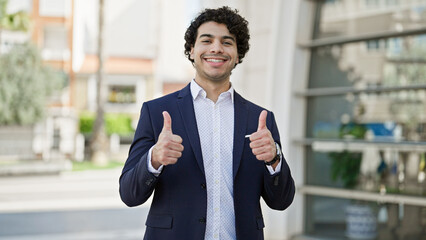 Canvas Print - Young latin man business worker smiling confident doing thumbs up gesture at street