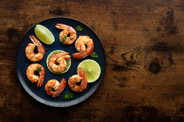 Wall Mural - Shrimps, overhead flat lay shot on a rustic wooden background with copy space. Grilled shrimp with lime, spicy seafood dish