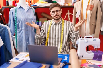 Poster - Hispanic man with beard using laptop at tailor room clueless and confused expression with arms and hands raised. doubt concept.