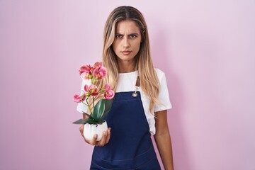 Wall Mural - Young blonde woman wearing gardener apron holding plant skeptic and nervous, frowning upset because of problem. negative person.