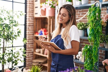 Poster - Young blonde woman florist smiling confident writing on notebook at florist