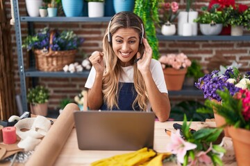 Wall Mural - Young blonde woman working at florist shop doing video call screaming proud, celebrating victory and success very excited with raised arm