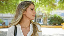 Cool And Relaxed Young Blonde Woman Standing Outdoors In A Sunny Park, Giving A Serious Sideways Glance - A Captivating Lifestyle Portrait In Nature