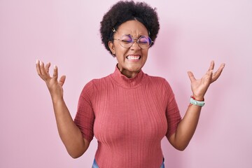 Wall Mural - Beautiful african woman with curly hair standing over pink background celebrating mad and crazy for success with arms raised and closed eyes screaming excited. winner concept