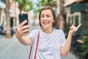 Poster - Middle age hispanic woman doing video call with smartphone smiling happy pointing with hand and finger to the side