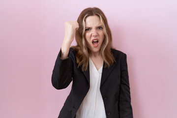 Poster - Young caucasian business woman wearing black jacket angry and mad raising fist frustrated and furious while shouting with anger. rage and aggressive concept.