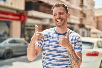 Sticker - Young hispanic man smiling confident doing ok sign with thumbs up at street