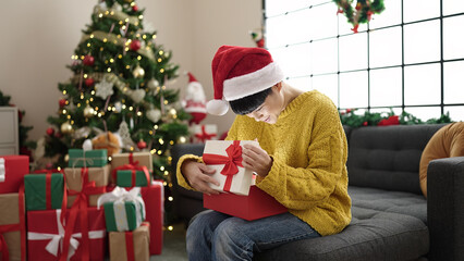 Wall Mural - Young chinese woman unpacking gift sitting by christmas tree at home