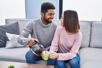 Canvas Print - Man and woman couple sitting on sofa pouring coffee on cup at home