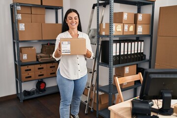 Poster - Young beautiful hispanic woman ecommerce business worker holding package at office