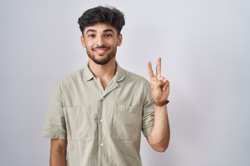 Sticker - Arab man with beard standing over white background showing and pointing up with fingers number two while smiling confident and happy.