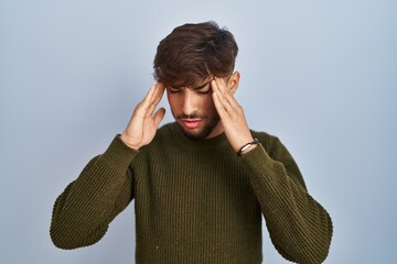 Poster - Arab man with beard standing over blue background with hand on head for pain in head because stress. suffering migraine.